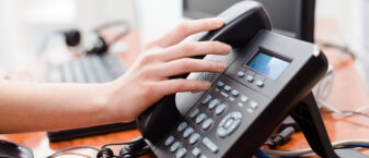 une main posée sur un téléphone fixe de bureau, prête à décrocher le combiné